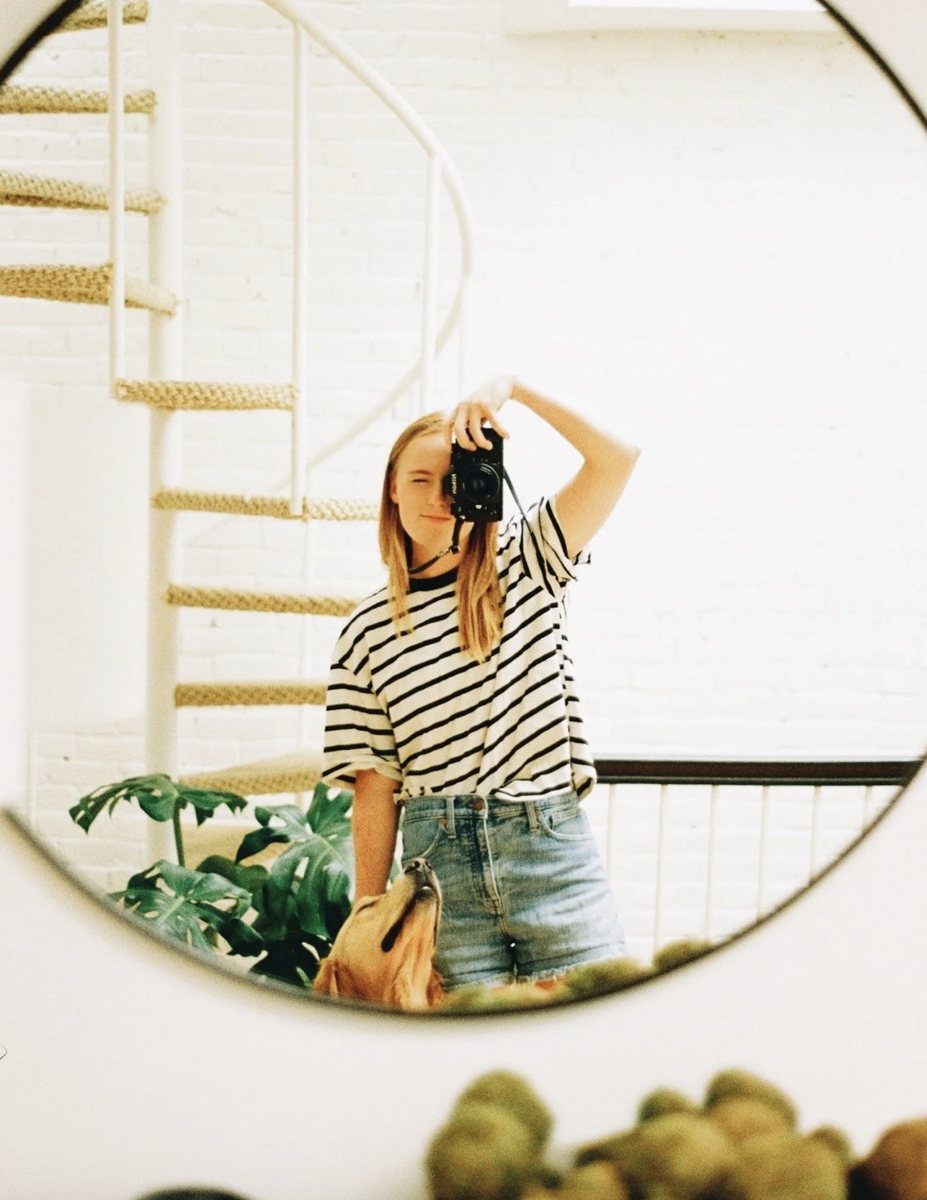 Kappy Arnold taking a photo of herself in a round mirror with a film camera, a golden retriever at her side