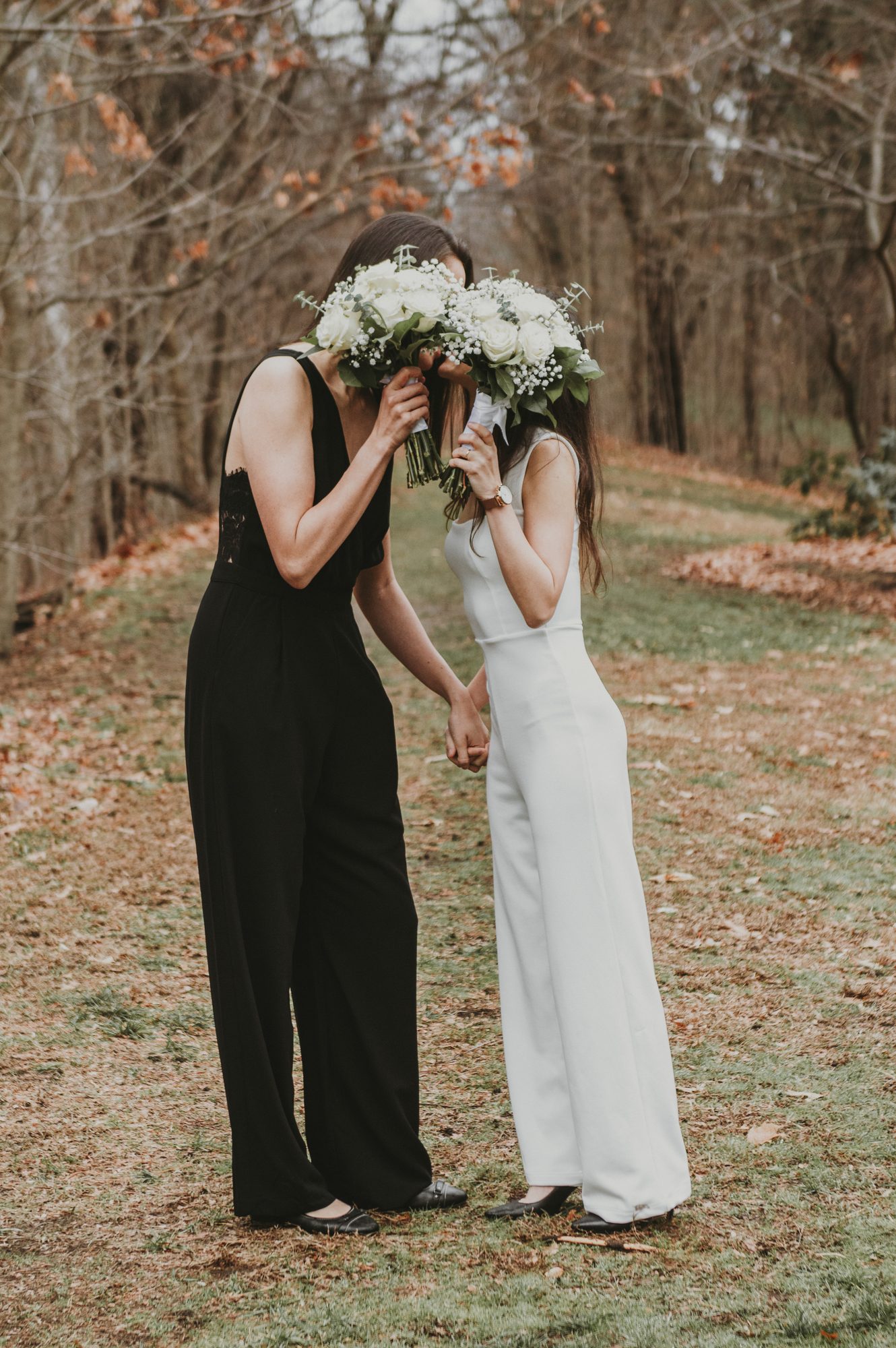 Two brides holding bouquets in front of their faces in an autumn wood