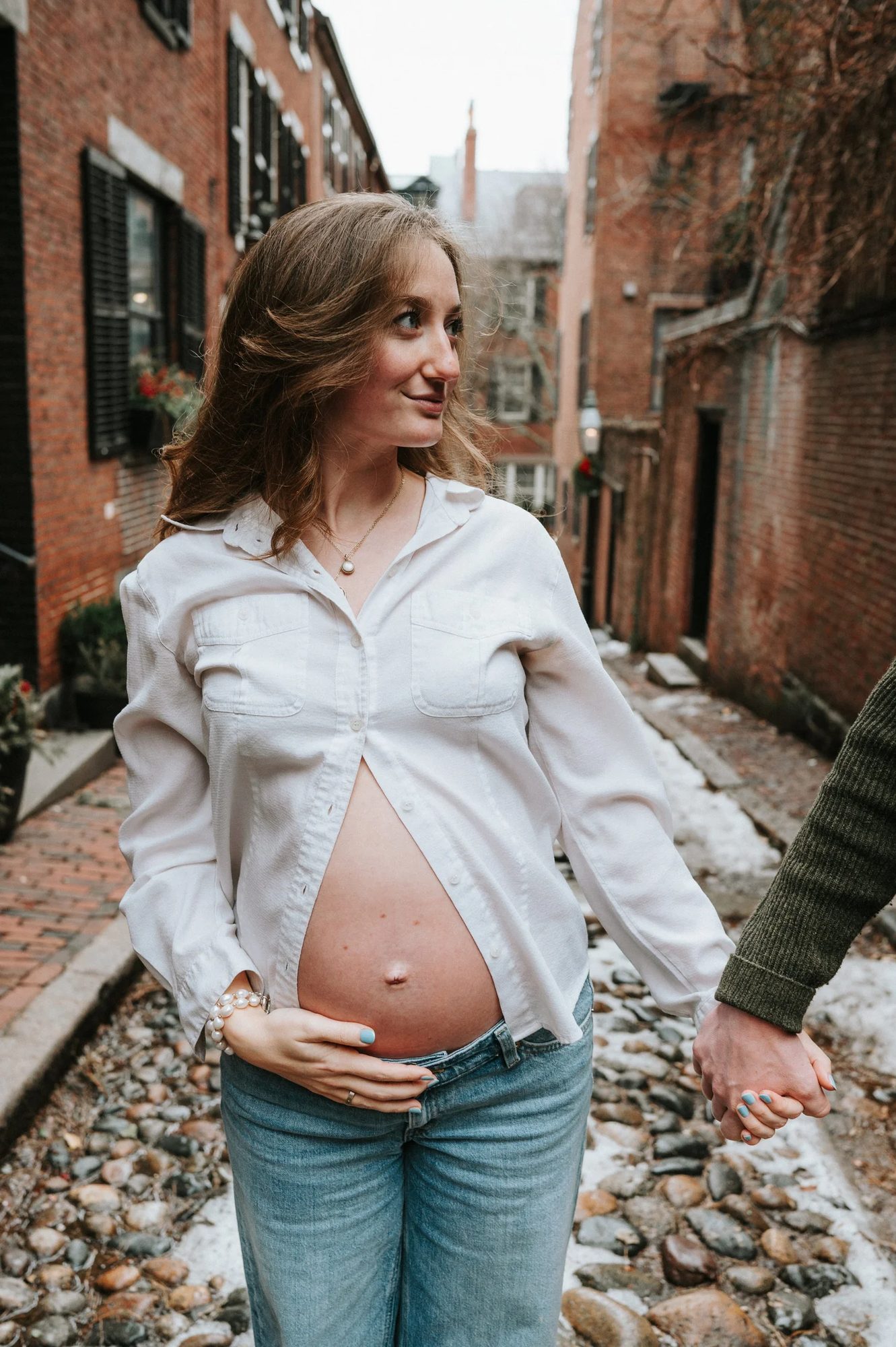 A pregnant woman in a white shirt on a brick-lined lane, holding someone's hand