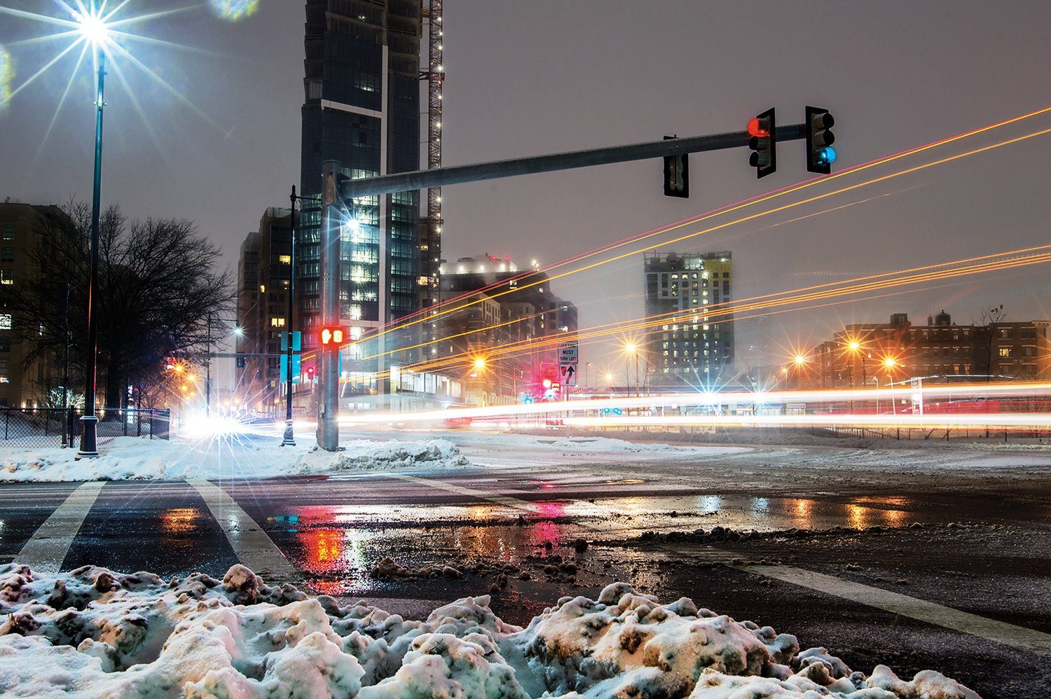 A city intersection at night with light trails and snow at the curb