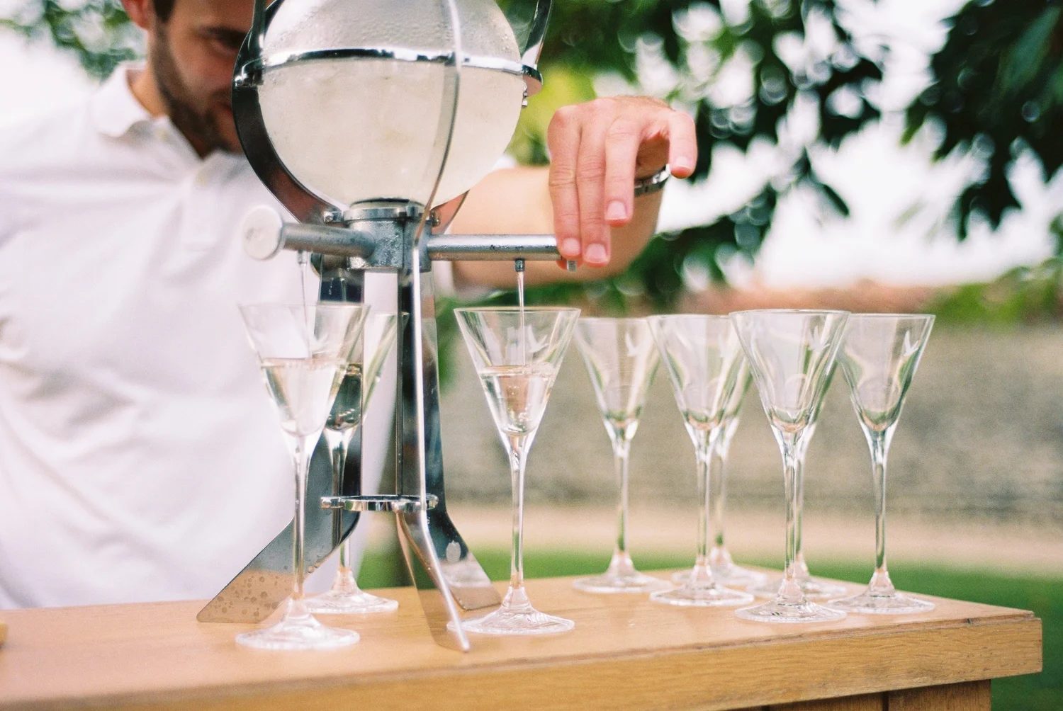 A man pouring from a glass dispenser into a row of coupe glasses