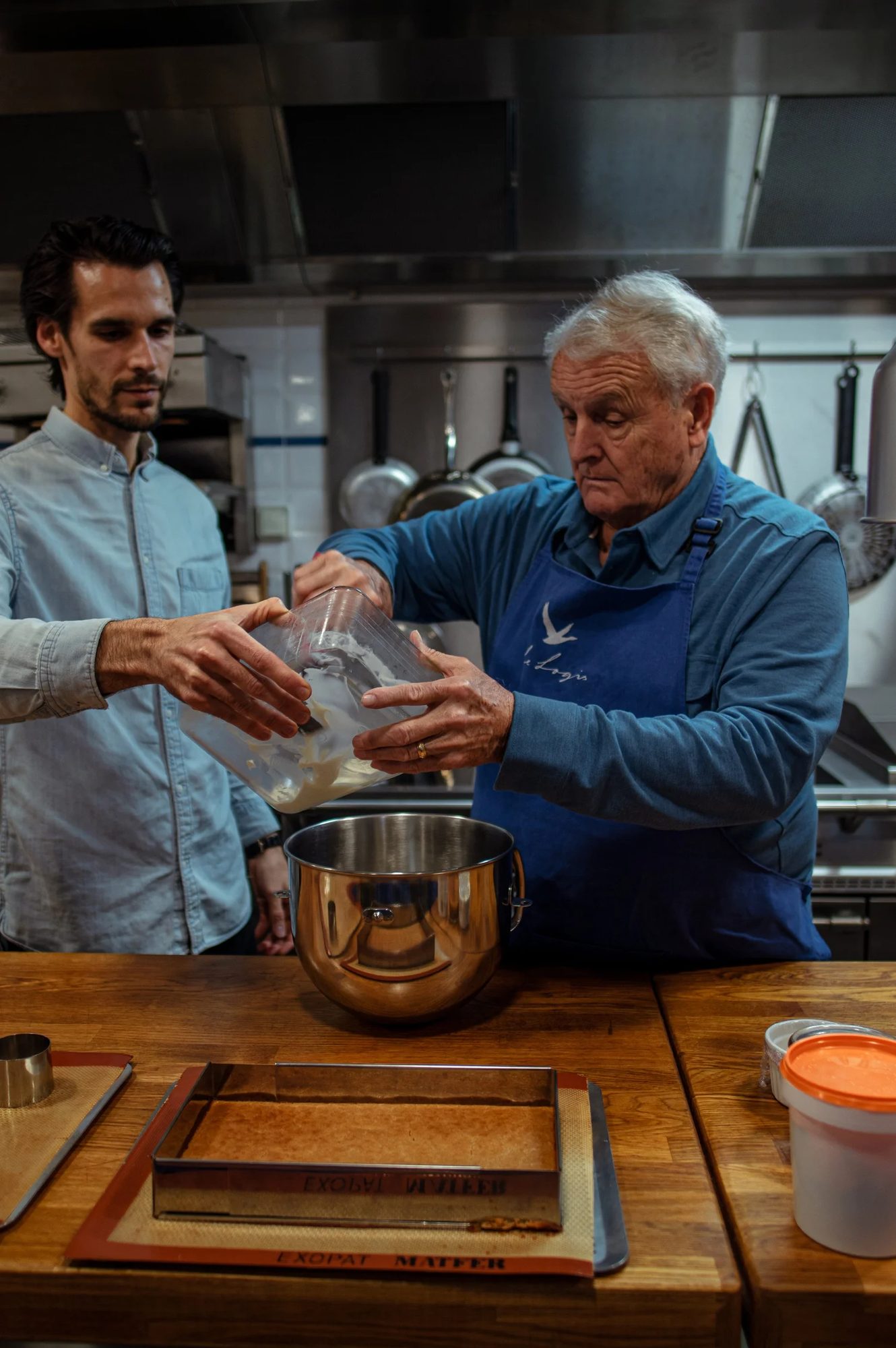 Two men cooking together over a steel bowl in a kitchen