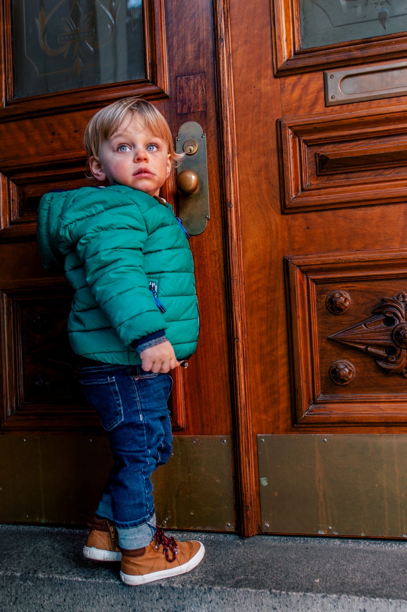 A small boy in a green jacket leaning against a carved wooden door